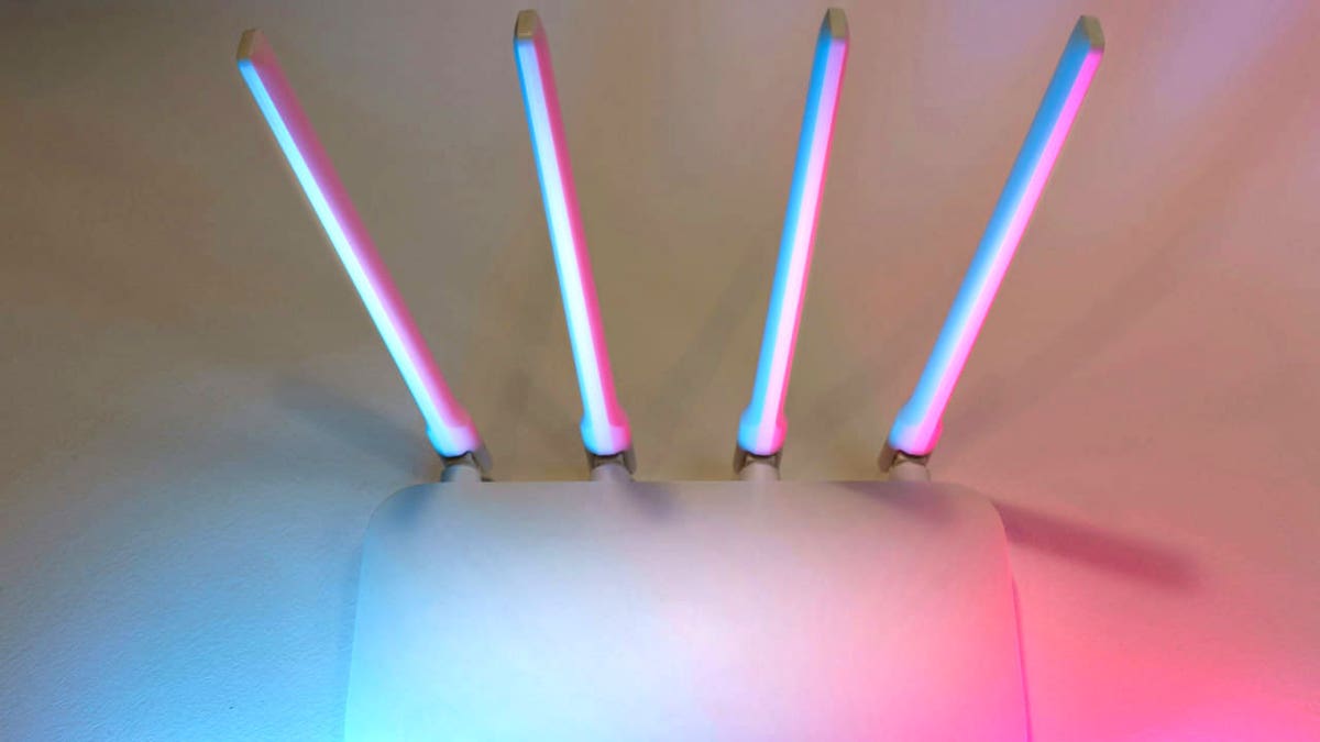 Wireless router with four antennas glowing in blue and pink light.
